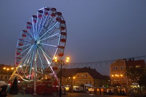 Podświetlona karuzela typu diabelski młyn, stojąca o zmierzchu na rynku miejskim. 