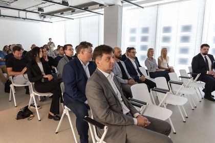 Zdjęcie przedstawia siedzących ludzi na konferencji w pomieszczeniu.