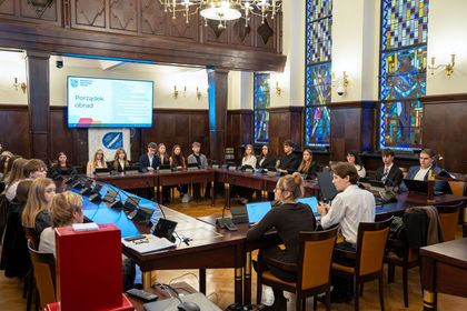 Grupa osób siedząca na sali sesyjnej. 