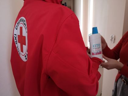 Ratownik medyczny stojący tyłem, odbiera plastikową butelkę od innej osoby