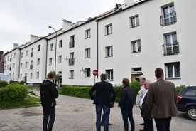 Grupa mężczyzn przechodzi obok jasnego dwupiętrowego budynku. 