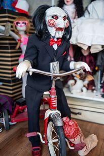 Zdjęcie przedstawia straszną lalkę na rowerze.
