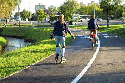Asfaltowa droga rowerowa wzdłuż rzeki, dziewczyna na rolkach, chłopak na rowerze
