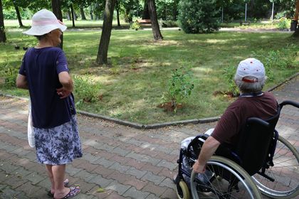 Dwie starsze osoby - jedna na wózku inwalidzkim - w ogrodzie