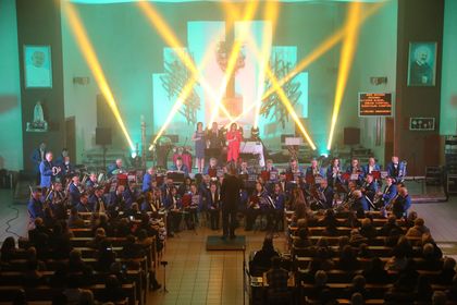 Muzycy Miejskiej Orkiestry Dętej Rybnik podczas koncertu kolędowego w kościele, na ołtarzu soliści, w ławkach publiczność. 