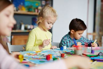 Trójka dzieci maluje i siedzi przy stoliku.