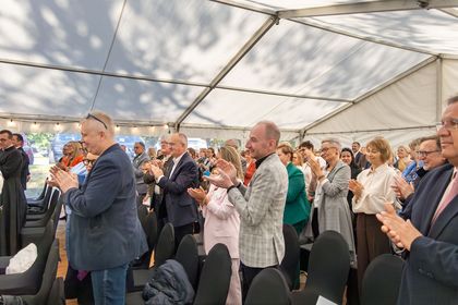 Na zdjęciu widać grupę ludzi, którzy stoją i klaszczą na oficjalnym wydarzeniu.