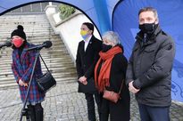 Kilka osób na otwartej przestrzeni, pod niebieskim namiotem. Na pierwszym planie dwóch mężczyzn i 2 kobiety w maseczkach. 