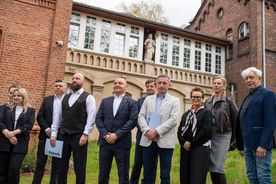 Zdjęcie przedstawia ludzi na tle budynku Juliusz