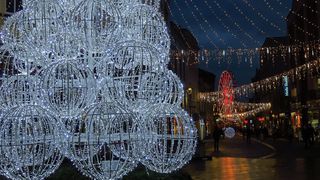 Wieczór. Świątecznie udekorowane miasto - lampki nad ulicami, choinki, i inne ozdoby.