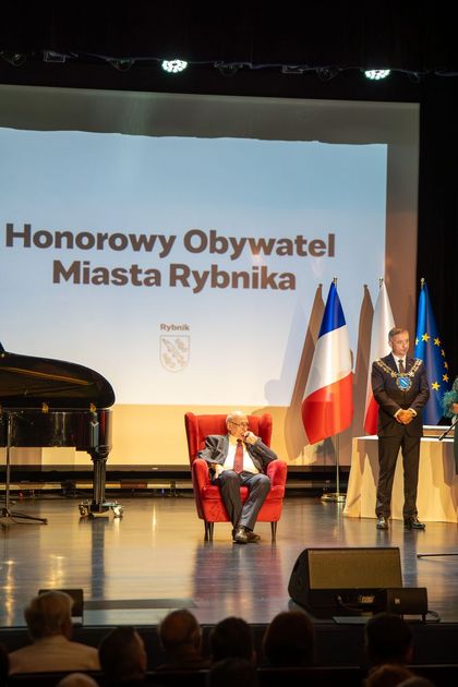 zdjęcie przedstawia honorowego obywatela Rynika siedzącego na scenie, obok stoi prezydent miasta