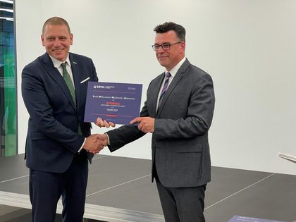 Dwaj mężczyźni w garniturach podają sobie ręce, jeden - zastępca prezydenta Rybnika - trzyma fioletowy certyfikat projektu SOWA