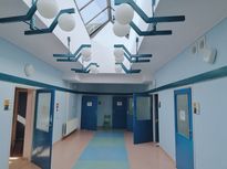 OsrodekJPII remont 3 Przestronny, jasny korytarz, po obu stornach otwarte drzwi w kolorze niebieskim, podwieszany sufit ze świetlikami okiennymi.