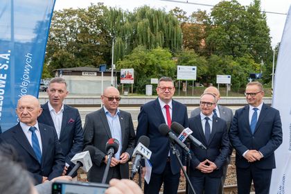 Zdjęcie przedstawia grupę mężczyzn stojących przy mikrofonach na peronie pkp.
