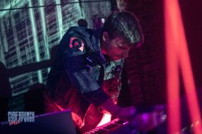 Mężczyzna w ciemnym ubraniu przy keyboardzie w trakcie koncertu. 