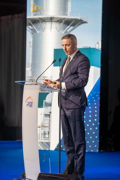 Mężczyzna stojący na scenie, mówiący do mikrofonu.