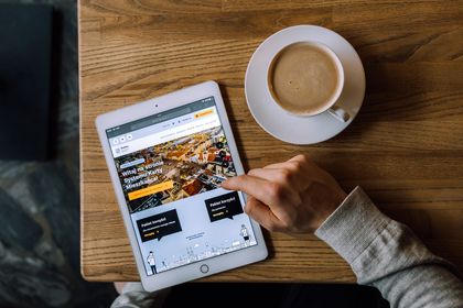 Stolik, na którym stoi kawa i tablet z wyświetloną stroną miasta Rybnika, widoczna też ręka obsługująca urządzenie 