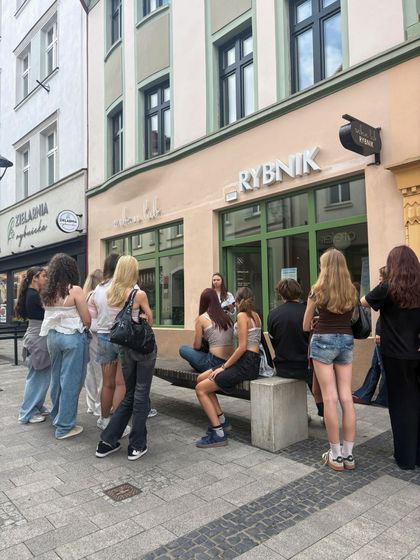 Zdjęcie przedstawia grupę ludzi stojących i siedzących przed wejściem do Urban Labu.