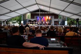 Widzowie siedzący przed oświetloną kolorowymi światłami sceną w ławkach - widok z tyłu na widownię. 