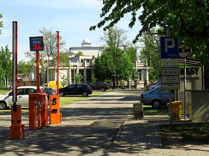 Parking bazylika fot L.Tyl 2 Samochody na parkingu. Na pierwszym planie bramka do poboru biletu parkingowego. W tle zieleń.