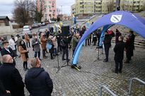 Kilkanaście ubranych zimowo osób na otwartej przestrzeni. Kilka osób stoi pod błękitnym namiotem z herbem miasta Rybnika. W tle bloki mieszkalne. 