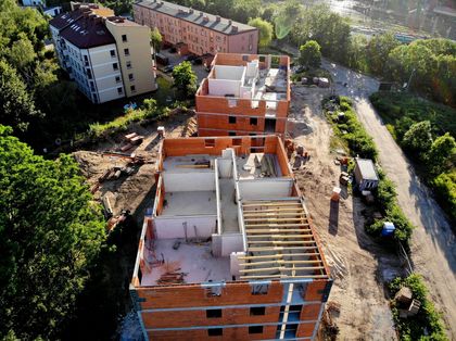 Budynki wielorodzinne w trakcie budowy. W tle istniejąca zabudowa i zieleń.