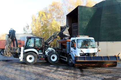 Ulice miasta, na nich pługopiaskarka i pracownicy służb komunalnych z szuflami do odśnieżania.