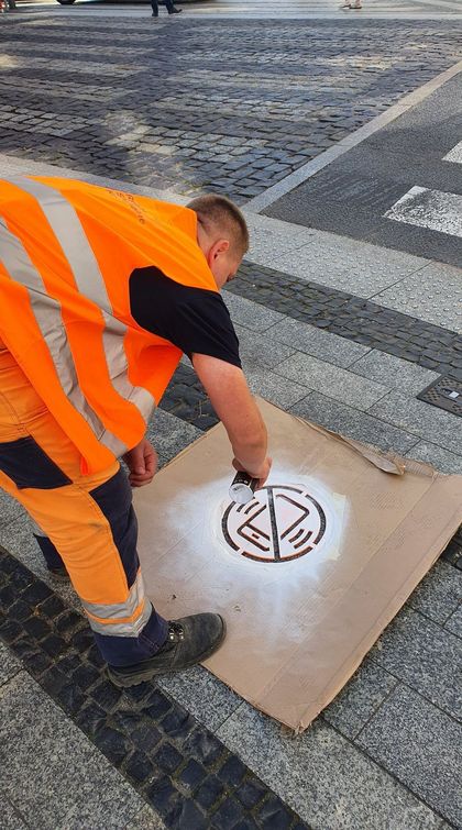 Mężczyzna w pomarańczowej kamizelce maluje poziomy znak drogowy przed przejściem dla pieszych