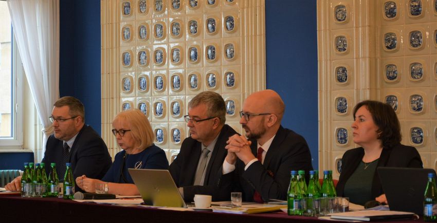 Pięć osób uczestniczących w spotkaniu. Siedzą za stołem. 