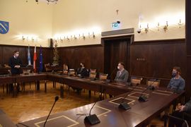 Wręczenie nagrody na sali galowej, przy stole cztery osoby, w tym trzech mężczyzn, , w tle flagi i herb miasta. 