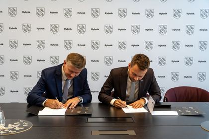 Zdjęcie przedstawia dwóch mężczyzn siedzących przy biurku. Mężczyźni podpisują dokumenty.