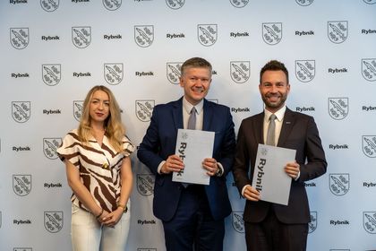 Zdjęcie przedstawia dwóch mężczyzn i kobietę pozujących do zdjęcia. Mężczyźni trzymają w rękach teczki z napisem Rybnik.