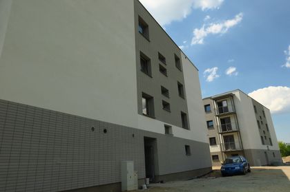 Jasne, kilkupiętrowe budynki mieszkalne z balkonami na tle błękitnego nieba z chmurami.