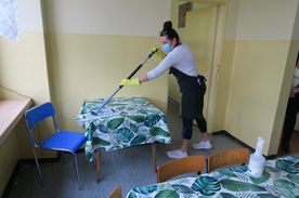 Kobieta myjąca mopem stolik na szkolnej stołówce