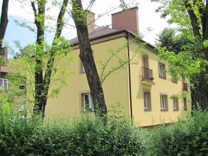 Wyremontowany pomalowany na jasny kolor budynek mieszkalny na tle zieleni i nieba. 