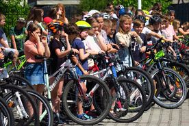 Grupa uczniów na rowerach i hulajnogach na placu szkolnym