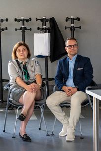 Zdjęcie przedstawia kobietę i mężczyznę, którzy siedzą w sali na spotkaniu.