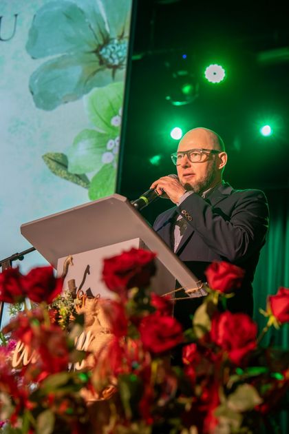 Mężczyzna stoi na scenie i mówi do mikrofonu.