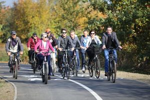 Asfaltowa droga rowerowa wzdłuż rzeki, drzewa, grupa rowerzystów