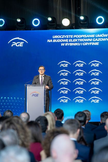 Mężczyzna stojący na scenie, mówiący do mikrofonu.