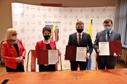 Dwie kobiety i dwóch mężczyzna prezentują podpisane dokumenty. W tle ścianka promocyjna z logosami. 