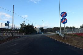 Skrzyzowanie ulicy z asfaltową drogą rowerową. Po prawej fragment wiaduktu oraz znaki drogowe informujące o końcu drogi dla rowerów.