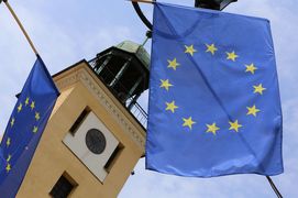 Fragment wieży ratusza, na jego tle dwie flagi Unii Europejskiej, niebieskie z żółtymi gwiazdami w kole. 