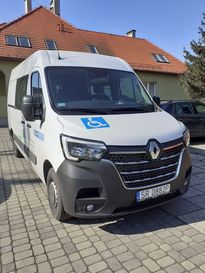 Biały bus do przewozu osób niepełnosprawnych, stojący przed budynkiem