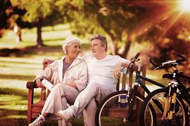 Dwójka seniorów - kobieta i mężczyzna siedzący na ławce. Obok dwa rowery