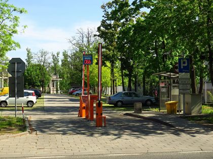 Parking bazylika fot L.Tyl 3 Samochody na parkingu. Na pierwszym planie bramka do poboru biletu parkingowego. W tle zieleń.