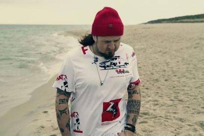 Mężczyzna w czerwone czapce i białej koszulce spacerujący brzegiem morza