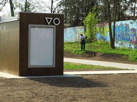 Budynek toalety miejskiej na skwerze. W tle mur z kolorowym grafitti