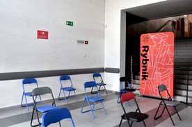 Korytarz, w którym stoi kilka krzeseł oraz czerwony baner z napisem Rybnik