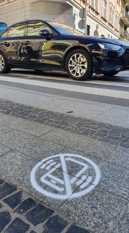 Poziomy znak drogowy przed przejściem dla pieszych - informujący o tym, aby nie korzystać z telefonu podczas przechodzenia przez pasy. W tle samochód. 